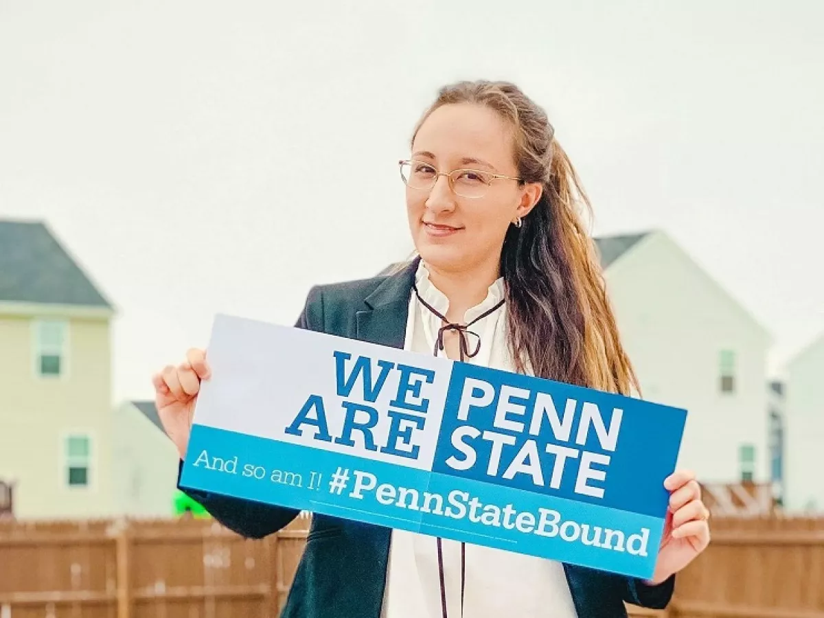 Woman with long hair and glasses holding sign saying "We Are Penn State"