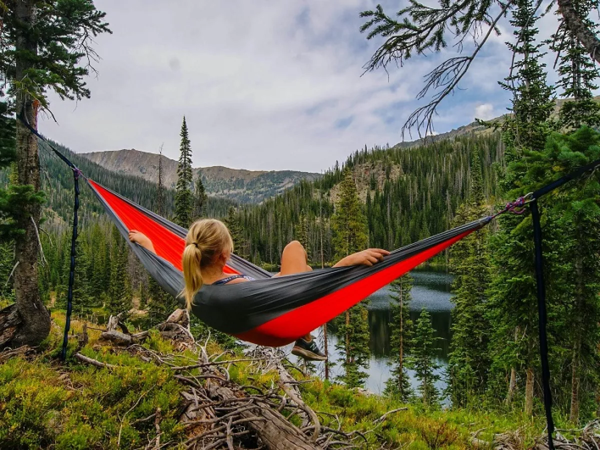 Woman relaxing in hammock near lake and mountains
