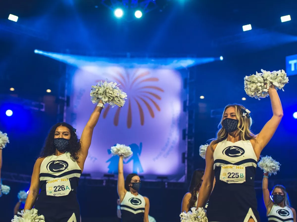 Penn State cheerleaders with raised arms holding pom poms at THON