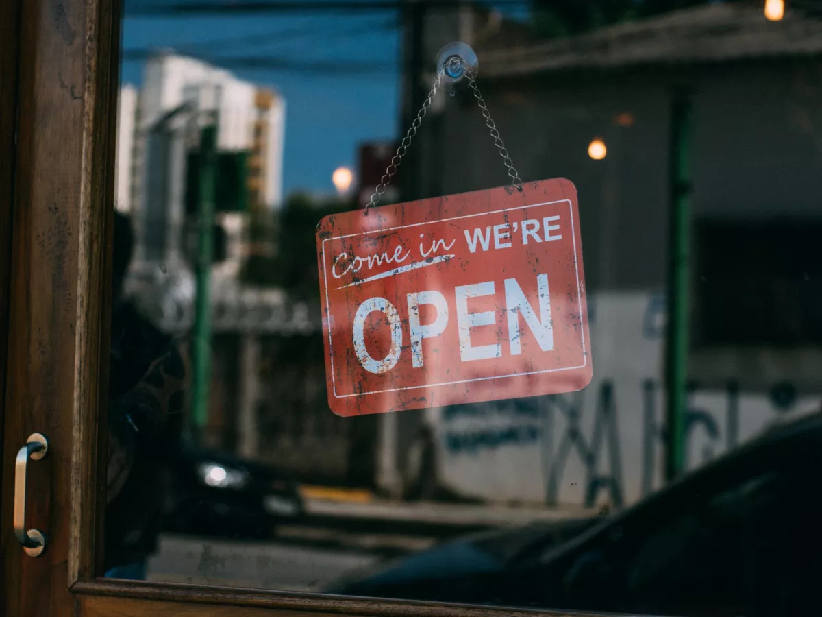 A sign that says, Come in, we are open, hangs in a business window