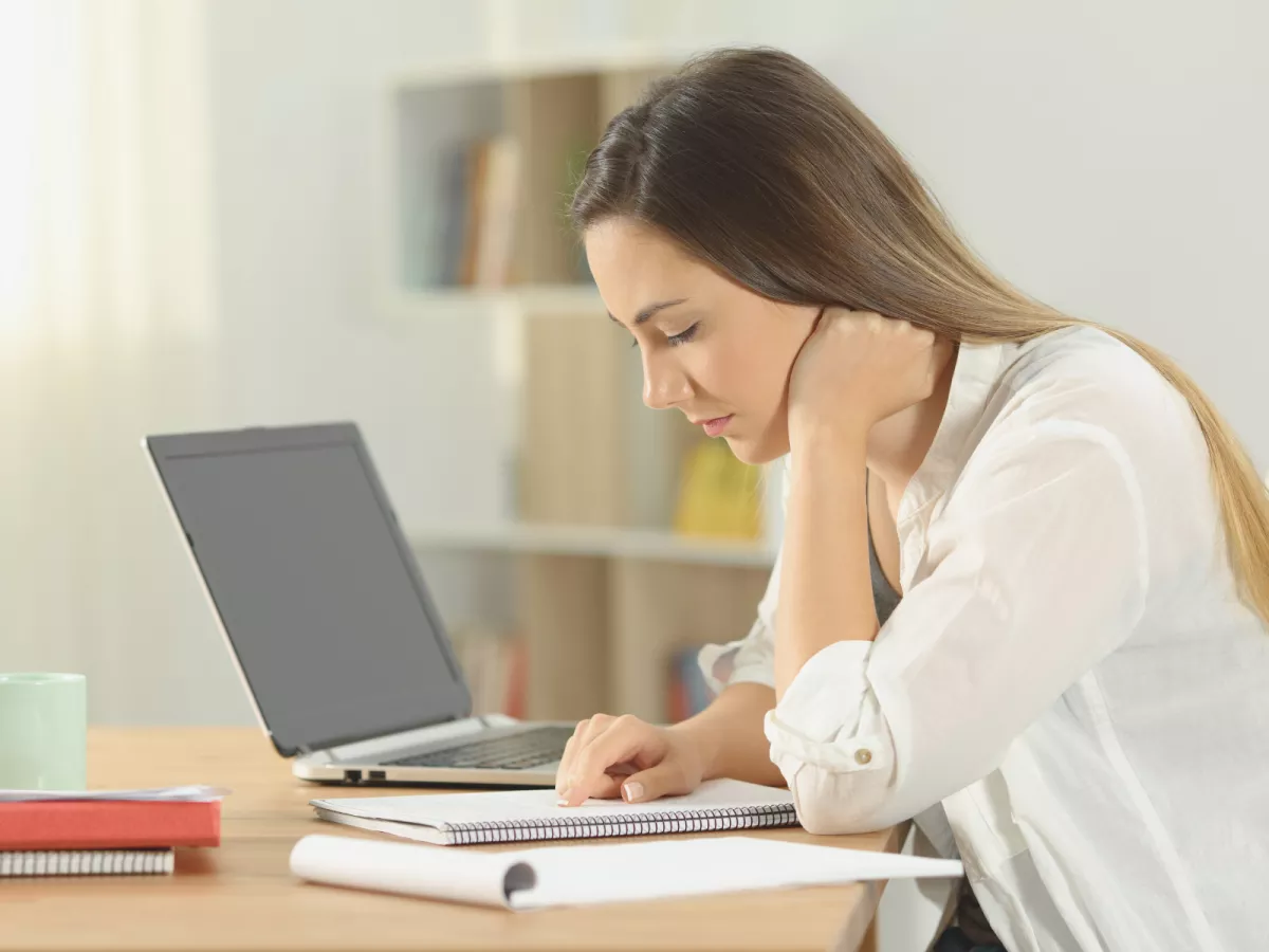 Woman with long dark hair looking down at a notebook with an open laptop nearby