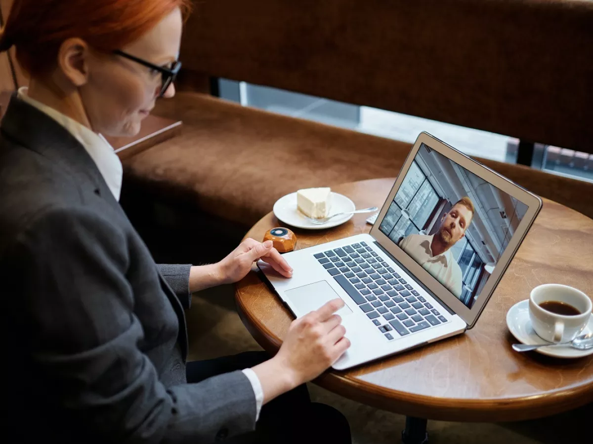 Woman using laptop and conducting virtual meeting with another person who appears on screen.