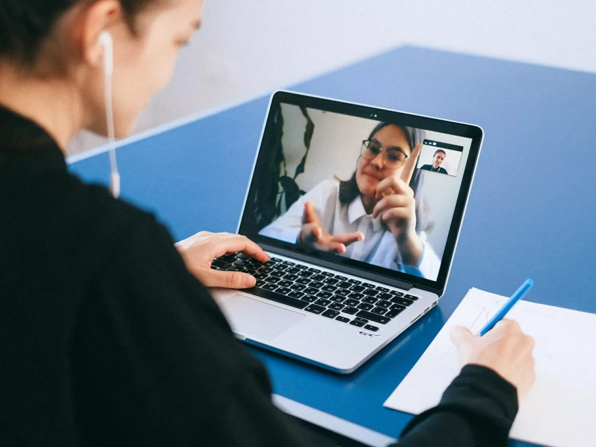 Person taking notes while looking at laptop screen where someone is explaining something with hand motions