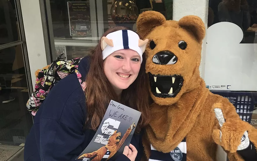 Smiling woman with long brown hair wearing Penn State gear standing next to the Nittany Lion mascot